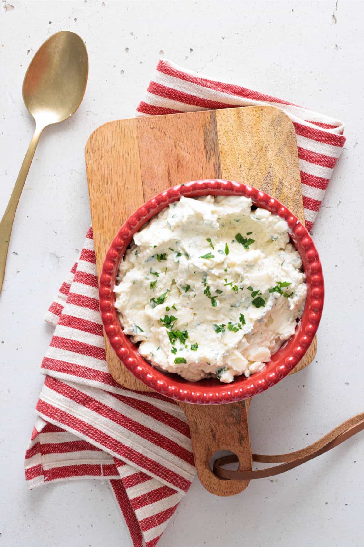 ricotta cheese mixture for lasagna and other baked dishes - in a red bowl with a spoon on the side on a wooden cutting board.