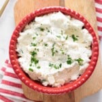 ricotta cheese mixture in a red bowl on a wooden cutting board with a kitchen napkin.