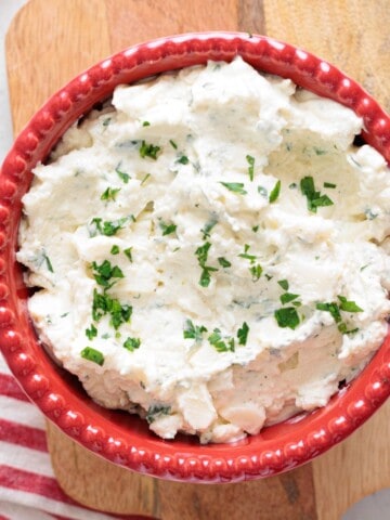 ricotta cheese mixture in a red bowl on a wooden cutting board with a kitchen napkin.