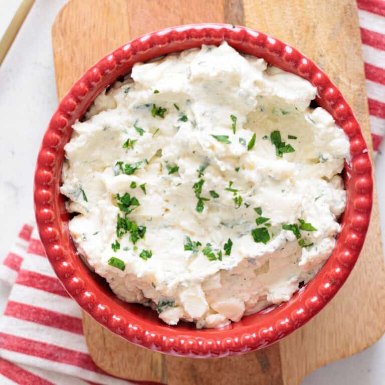 ricotta cheese mixture in a red bowl on a wooden cutting board with a kitchen napkin.