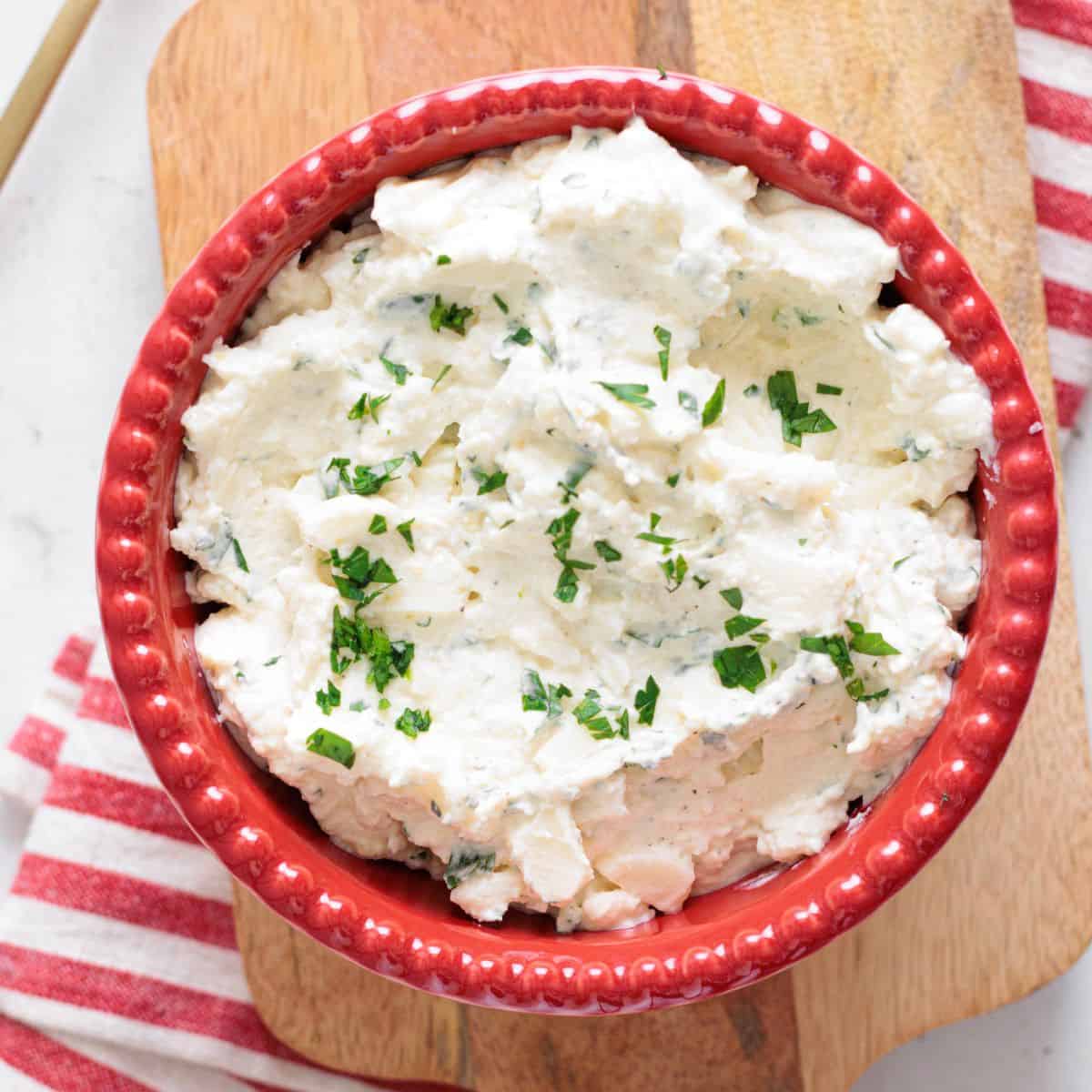 ricotta cheese mixture in a red bowl on a wooden cutting board with a kitchen napkin.