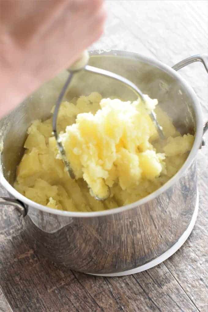Mashing Potatoes and milk with a potato masher in a pot