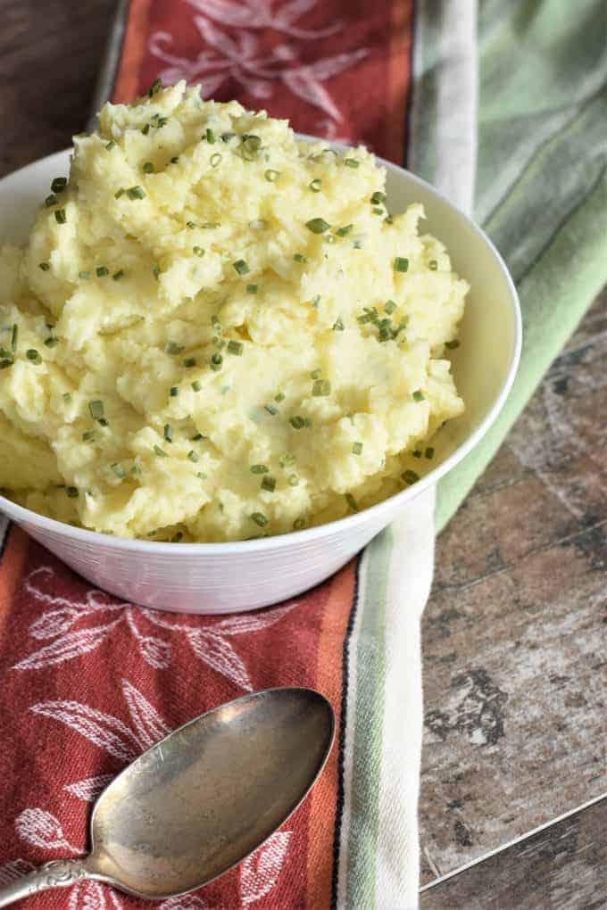 front view of mashed potatoes in a white bowl topped with chives with part of left side of the bowl cut off
