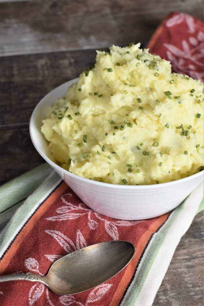 mashed potatoes in a white bowl with part of the right side cut off and a spoon in the front