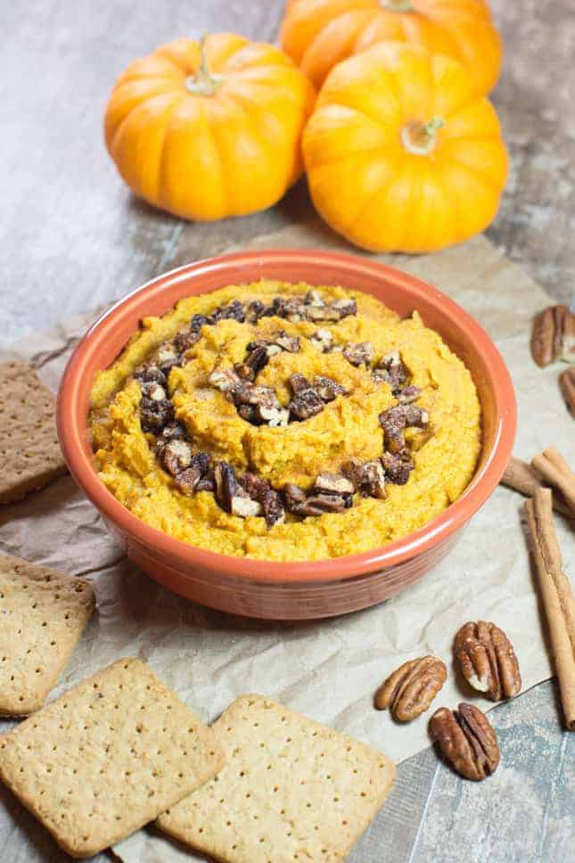 Pumpkin pie hummus in orange bowl with grahams, pecans and cinnamon sticks surrounding