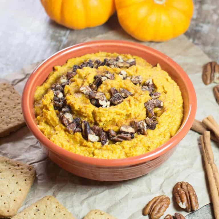 hummus in an orange bowl with grahams, pecans, cinnamon sticks and pumpkins around it
