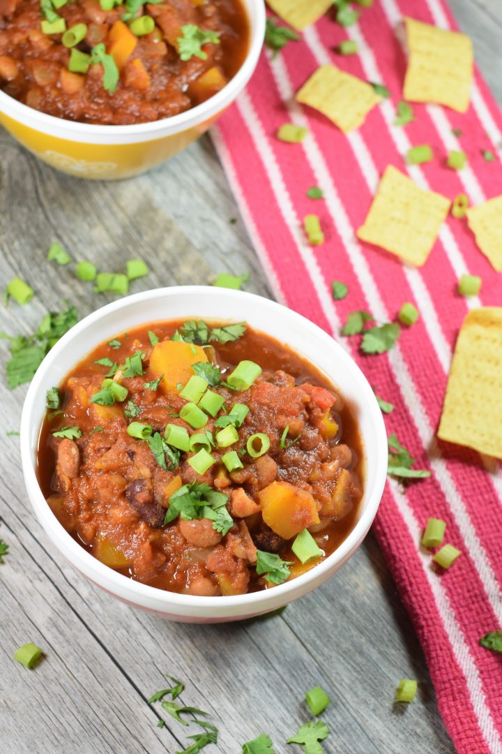 Slow Cooker Vegetarian Chili in two bowls with tortilla chips next to them and cilantro and parsley garnish
