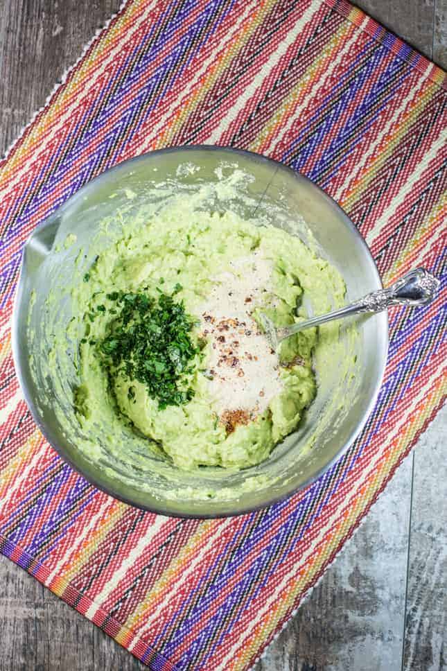 mashed avocado and seasonings in a mixing bowl with a spoon.
