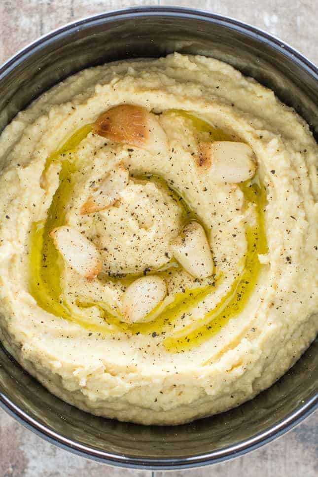 close-up overhead of hummus in bowl garnished with garlic, olive oil and black pepper