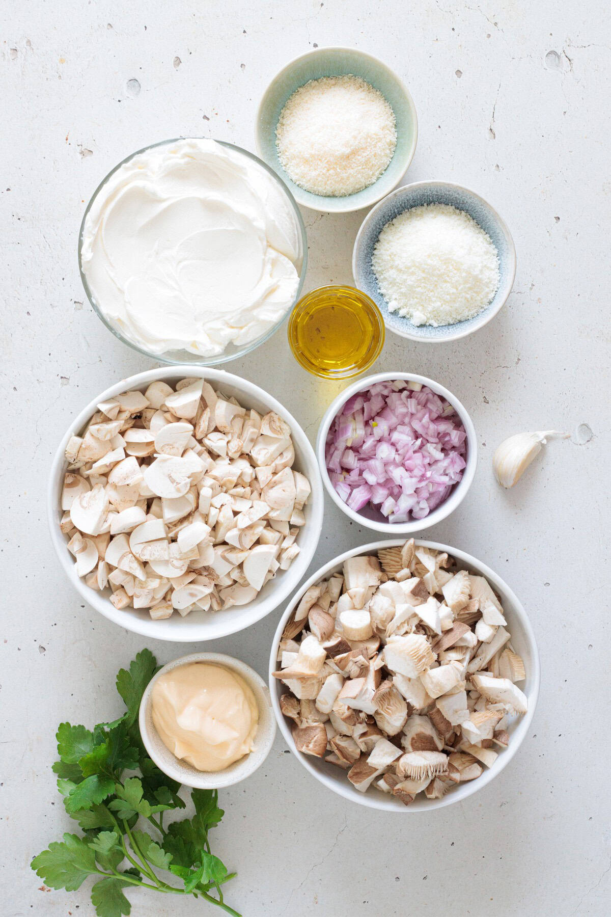 Overhead pic of creamy mushroom dip ingredients including button mushrooms, oyster mushrooms, cream cheese, sour cream, mayo, parmesan, shallots, garlic, olive oil, and fresh parsley