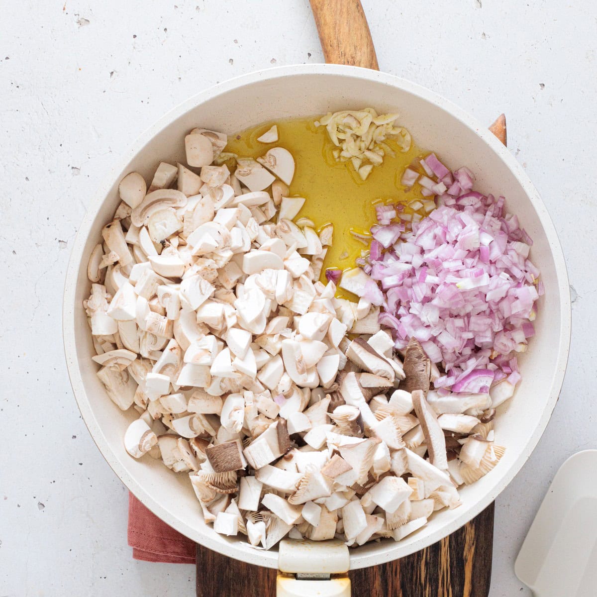Chopped button mushrooms, diced red onion, and minced garlic added to a white pan with olive oil to start the creamy mushroom dip