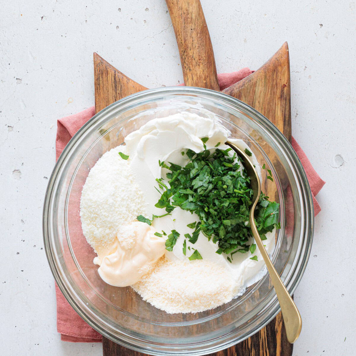 Glass bowl with cream cheese, sour cream, mayo, parmesan, and fresh chopped parsley combined as the base for creamy mushroom dip
