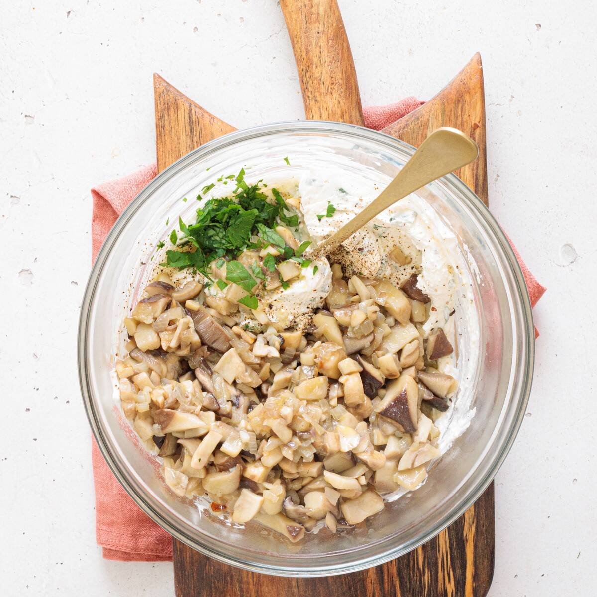 Saut&eacute;ed mushrooms folded into the cream cheese mixture in a glass bowl to make the creamy mushroom dip filling