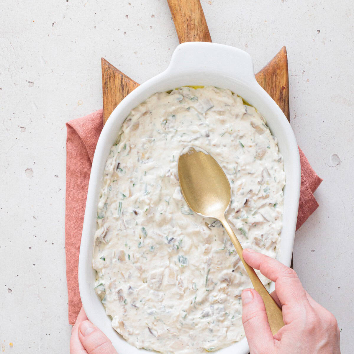 Creamy mushroom dip mixture spread evenly into a white oval baking dish, ready to be topped with parmesan