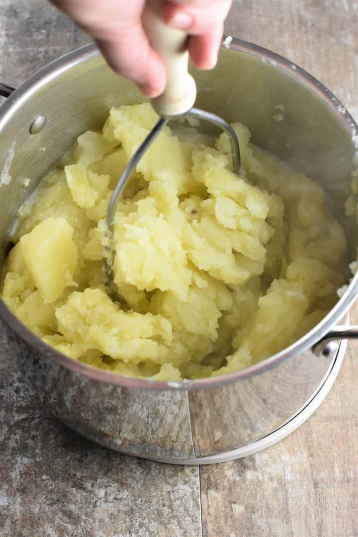 mashing potatoes with a potato masher in a pot
