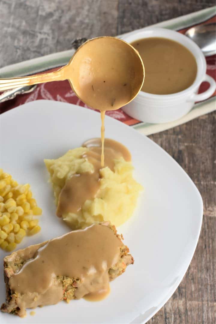 Ladling gravy onto mashed potatoes next to a piece of vegan chickpea veggie loaf with gravy on it too