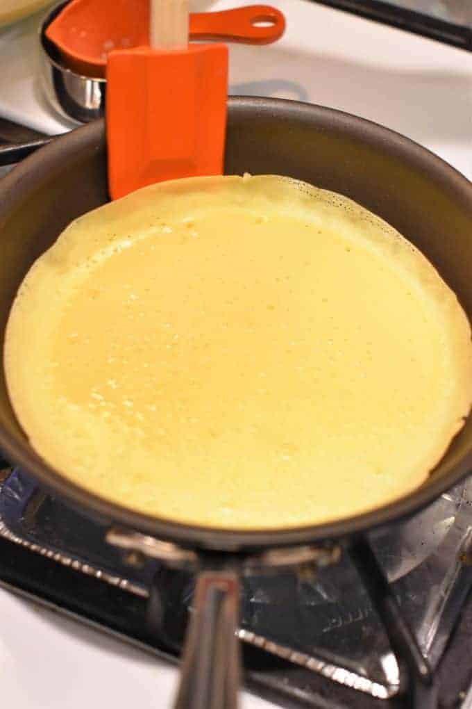 Using a spatula to prepare to flip the manicotti (crepe) shell in the pan
