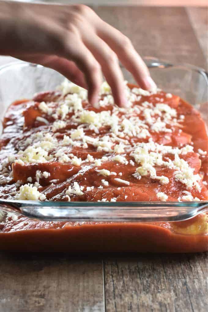 Sprinkling mozzarella cheese on top of manicotti in a glass baking dish