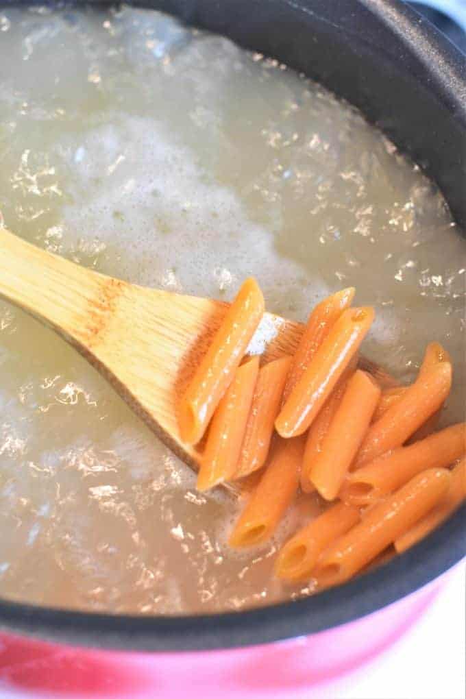 Wooden spoon scooping pasta out of boiling water