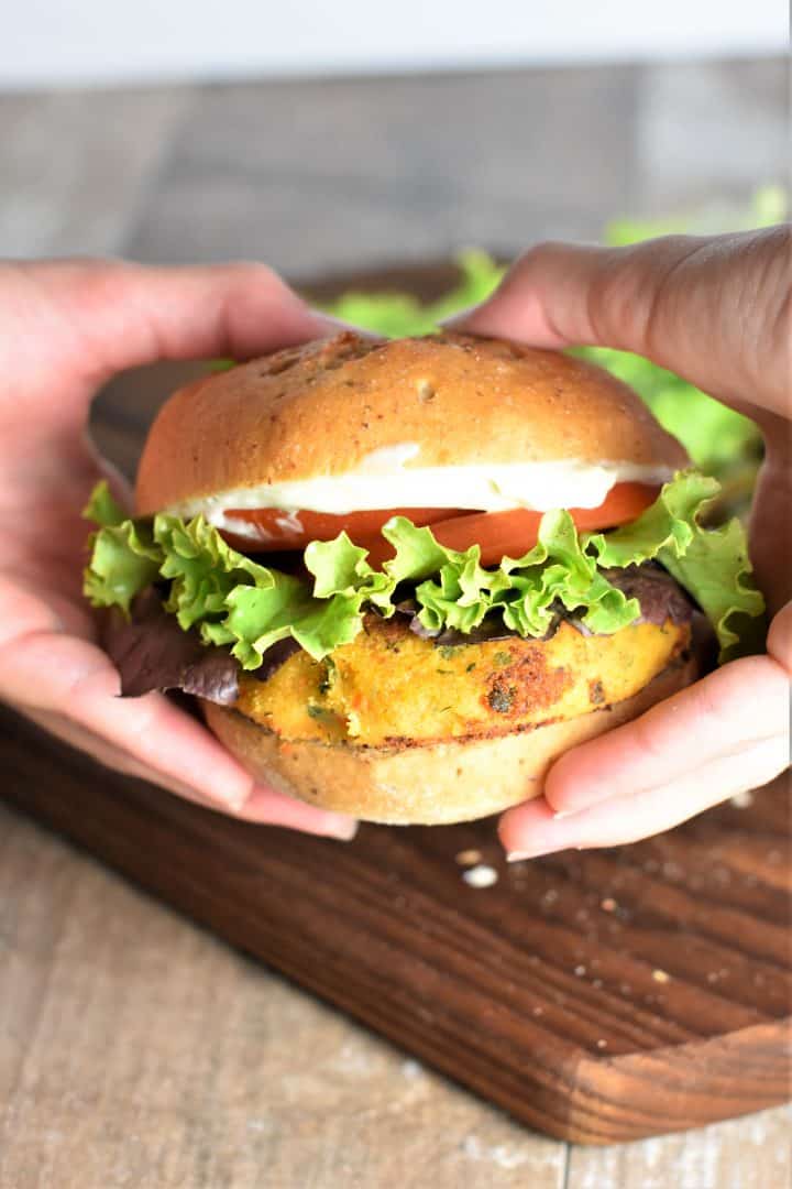 Veggie burger on a bun with lettuce tomatoes and mayo being held by hands