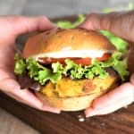 Veggie burger on a bun with lettuce tomatoes and mayo being held by hands
