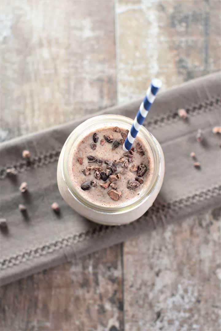 overhead of smoothie in mason jar with a straw in it topped with cacao nibs