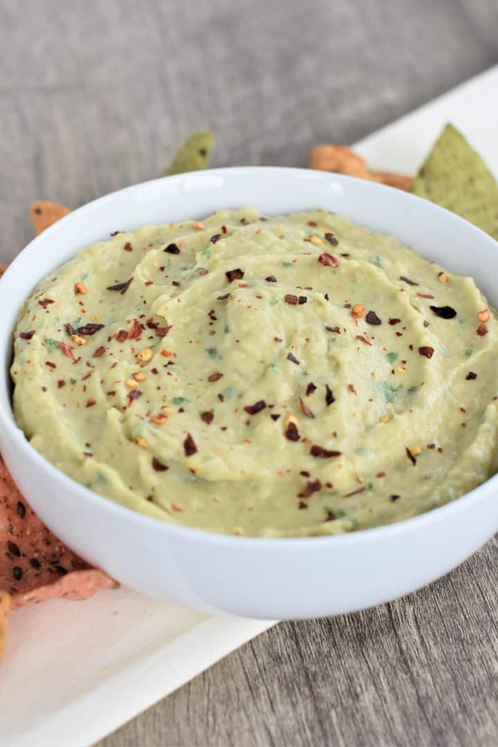 front view of hummus in a white bowl with tortilla chips around it