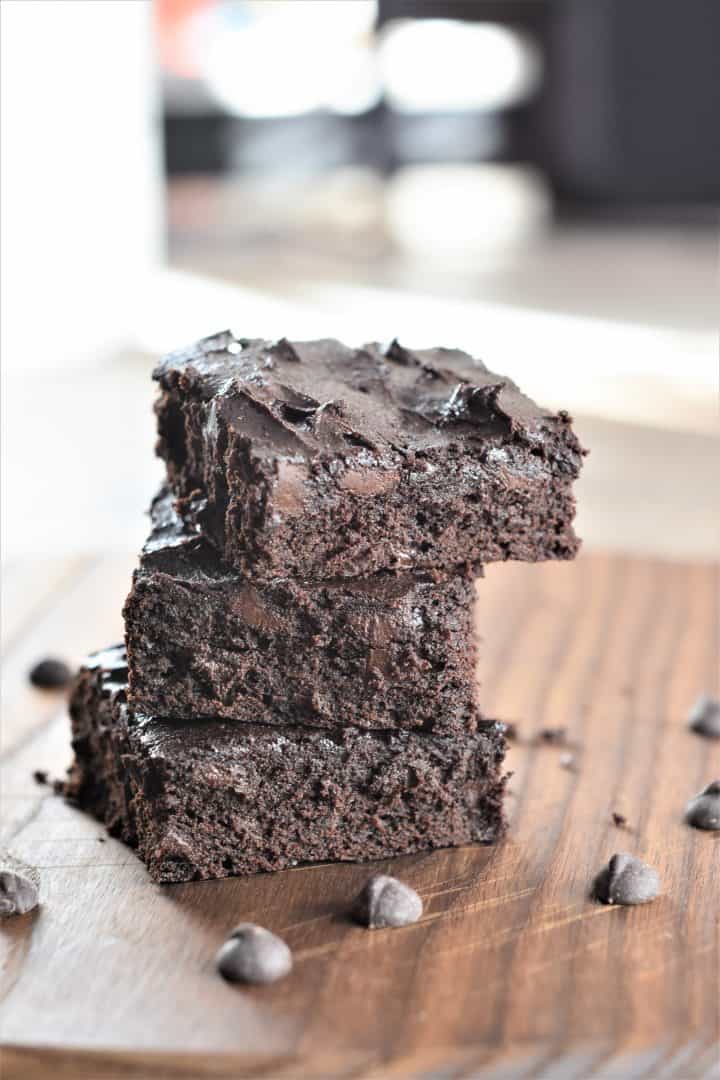 front view of 3 stacked brownies on wooden board with chocolate chips around
