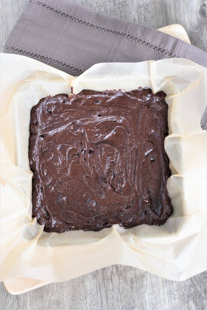 brownie batter in square baking dish lined with parchment