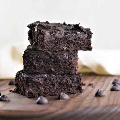 stacked brownies on a wooden board with chocolate chips around
