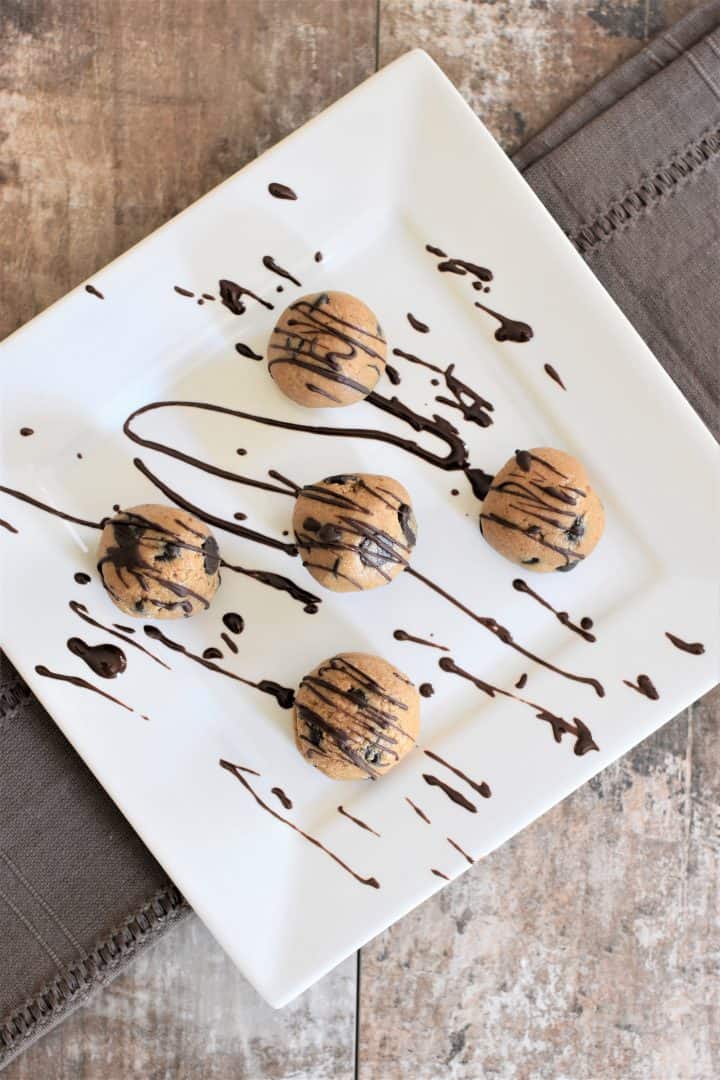 overhead of cookie dough balls on a white plate covered with chocolate drizzle