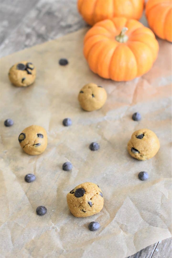 a few pumpkin bites on parchment paper with some chocolate chips around and mini pumpkins in the background