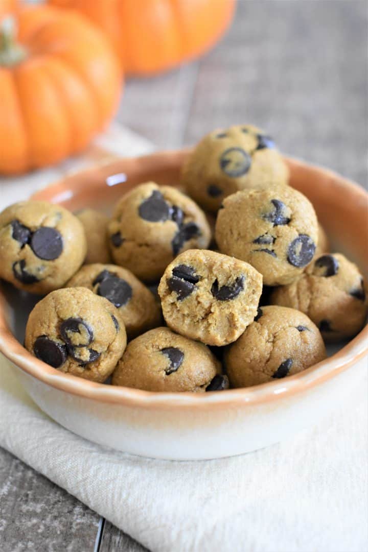 front view of pumpkin chocolate chip cookie dough bites in a bowl with a bite taken out of one 