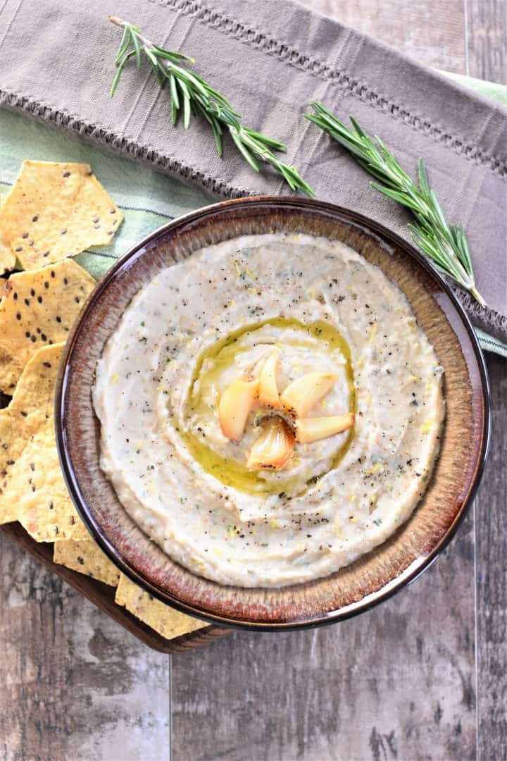 overhead of dip in a brown bowl with tortilla chips and rosemary sprigs on sides