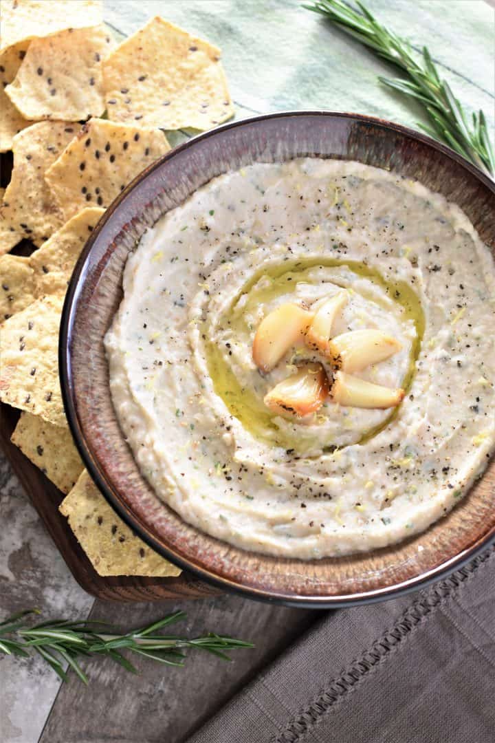 overhead of roasted garlic white bean dip in brown bowl with tortilla chips on the side
