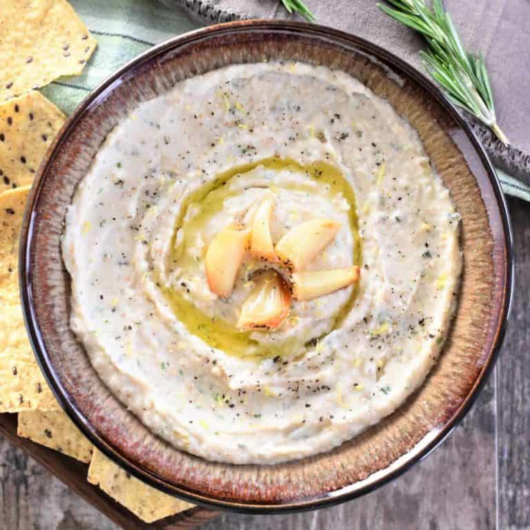 Overhead close-up of dip in a brown bowl with tortilla chips and rosemary sprigs on the side