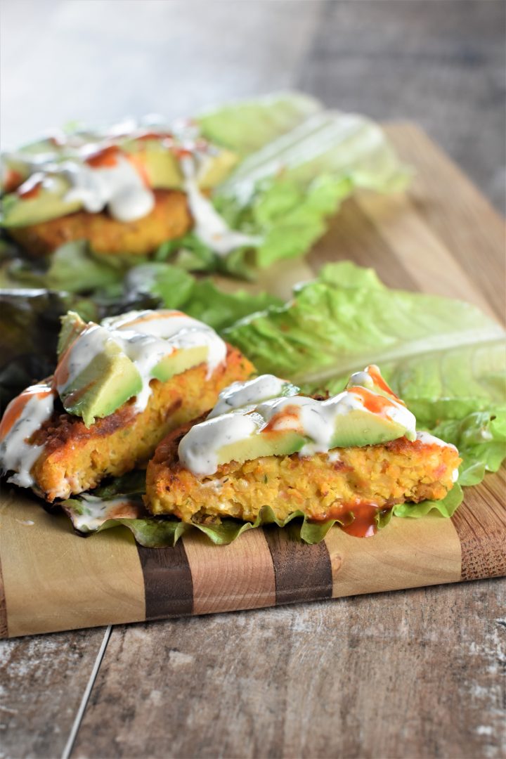 Vegan Buffalo Chickpea Burgers on lettuce with ranch dressing and avocado with front one cut open