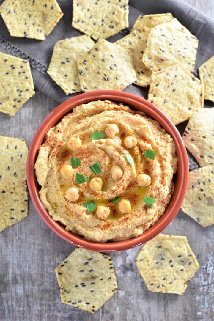 Overhead view of hummus without tahini in a red bowl with tortilla chips around it