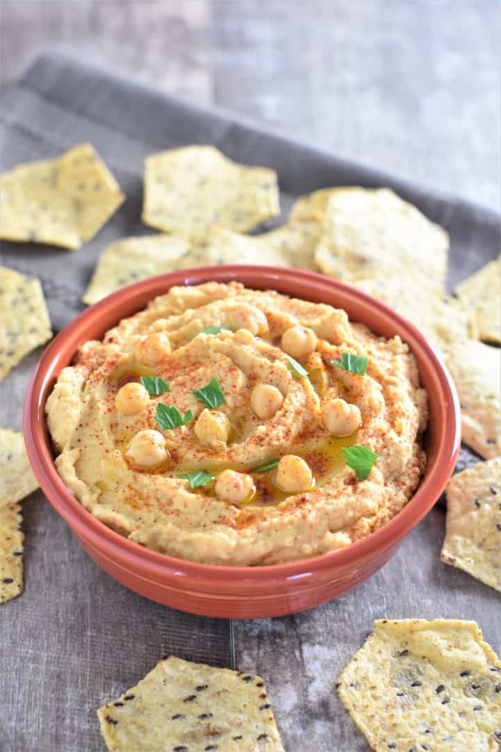 Hummus in a red bowl garnished with chickpeas and with tortilla chips around it