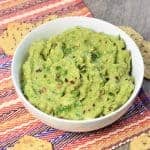 guacamole in a white bowl with chips around it