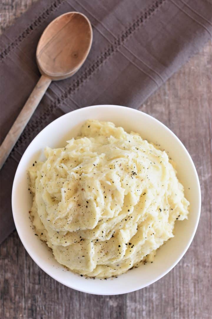 overhead shot of mashed potatoes in a white bowl with wooden spoon next to them