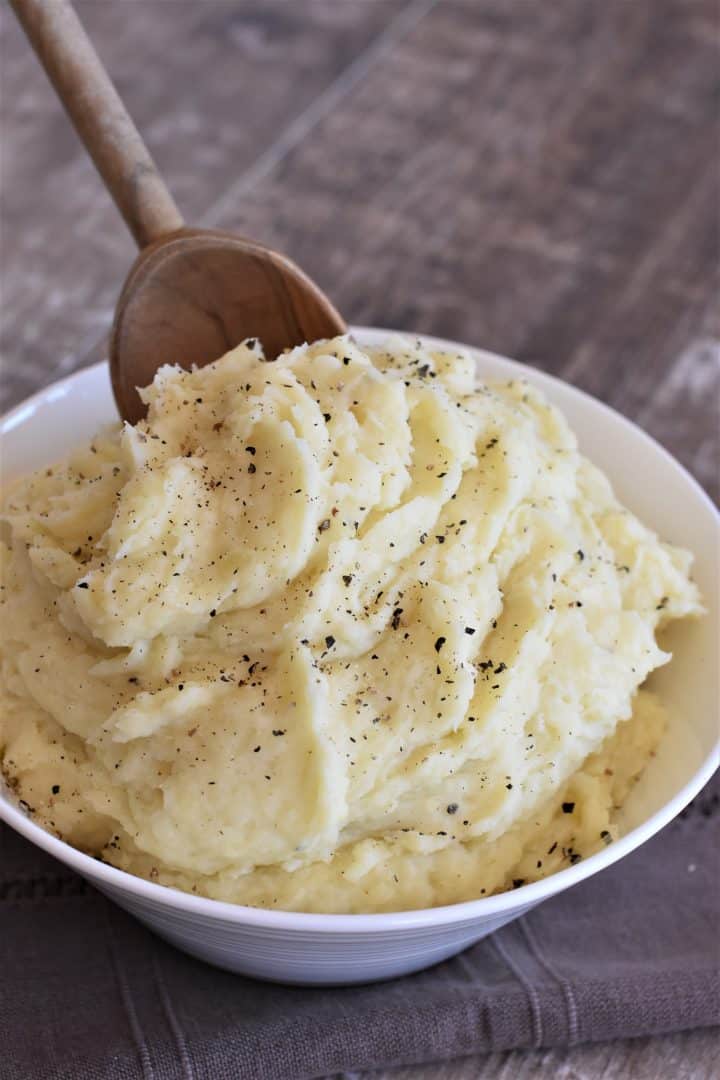 mashed potatoes in a white bowl with a wooden spoon dipping in