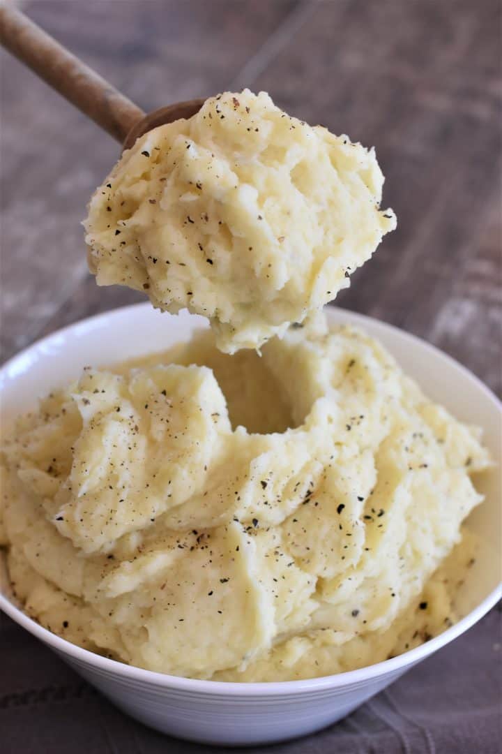A big scoop of mashed potatoes on a wooden spoon over the bowl of mashed potatoes