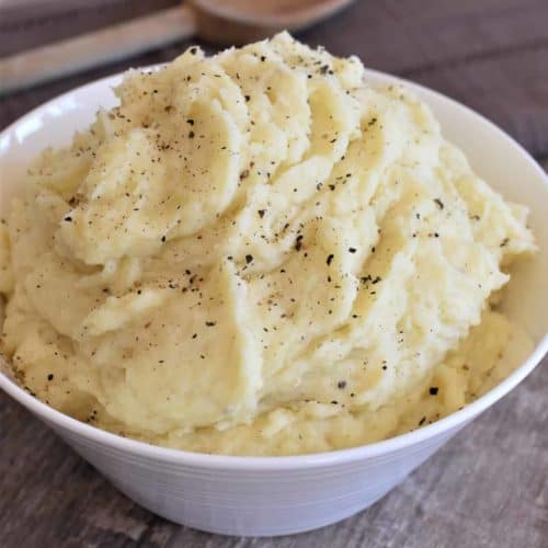 mashed potatoes in a white serving bowl with a wooden spoon behind it