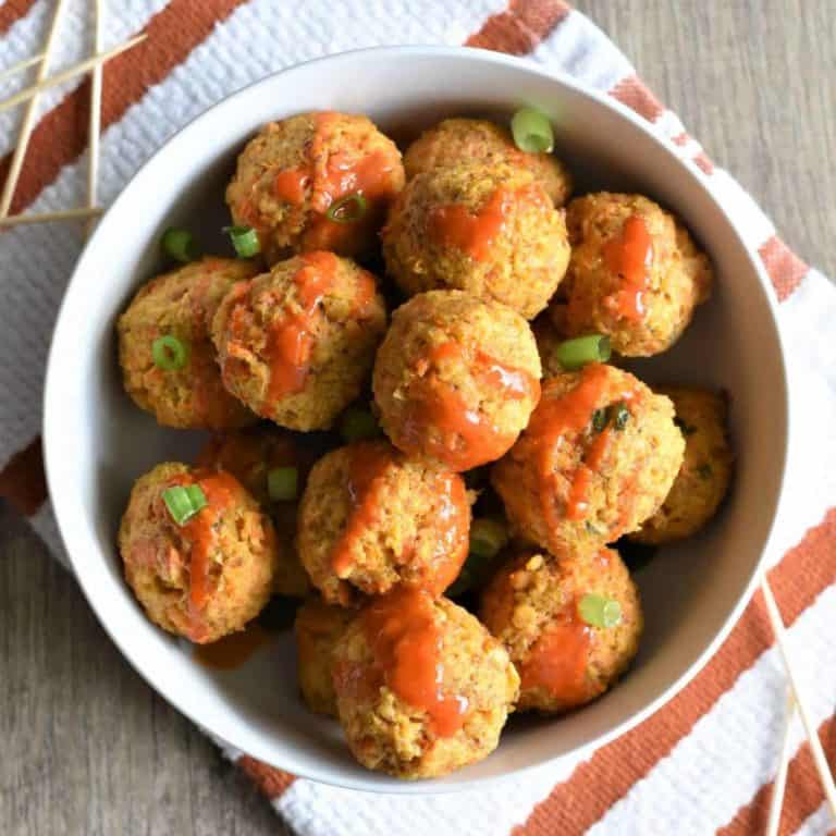 Overhead of chickpea balls topped with buffalo sauce and green onions in a white bowl