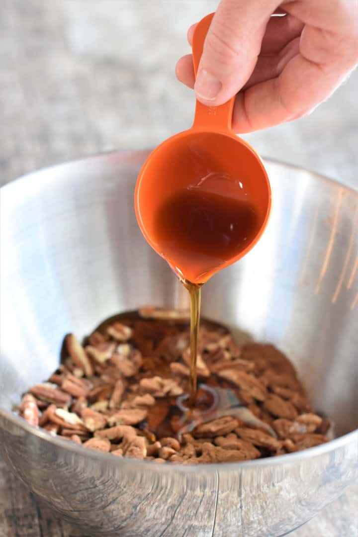 Pouring maple syrup onto the nuts in a mixing bowl