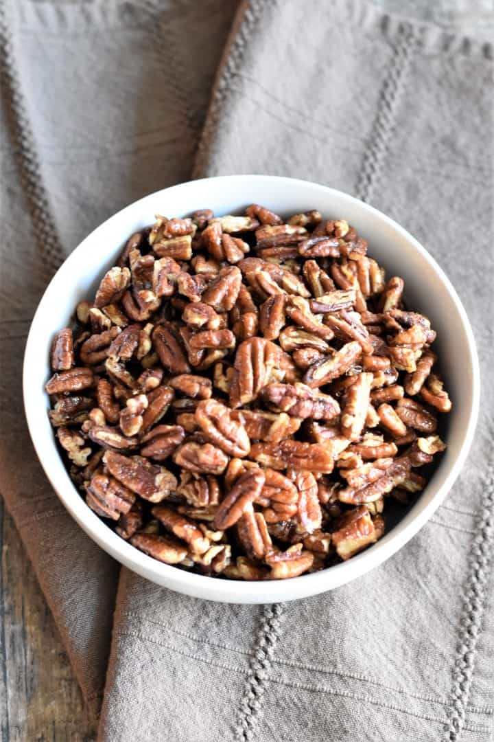 maple pecans in white bowl on a brown kitchen towel
