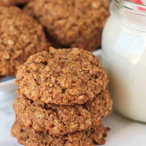 stack of three oatmeal cookies with glass of milk somewhat in view next to them