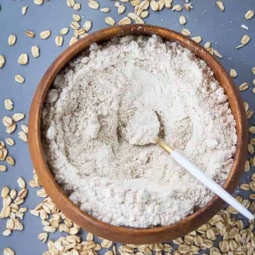 overhead of homemade oat flour in a bow with a spoon in it and oats around it