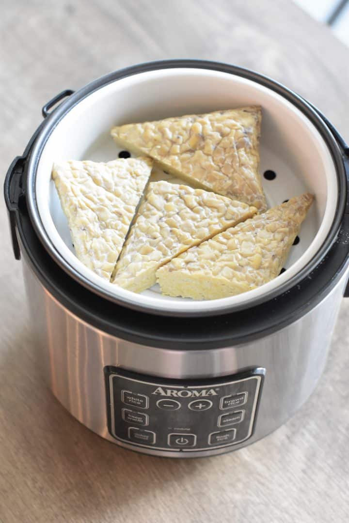 tempeh triangles added to steamer basket in a rice cooker